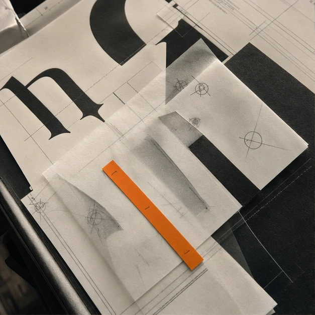 Layered typographic proofs, tracing paper, registration marks, and a narrow orange correction strip